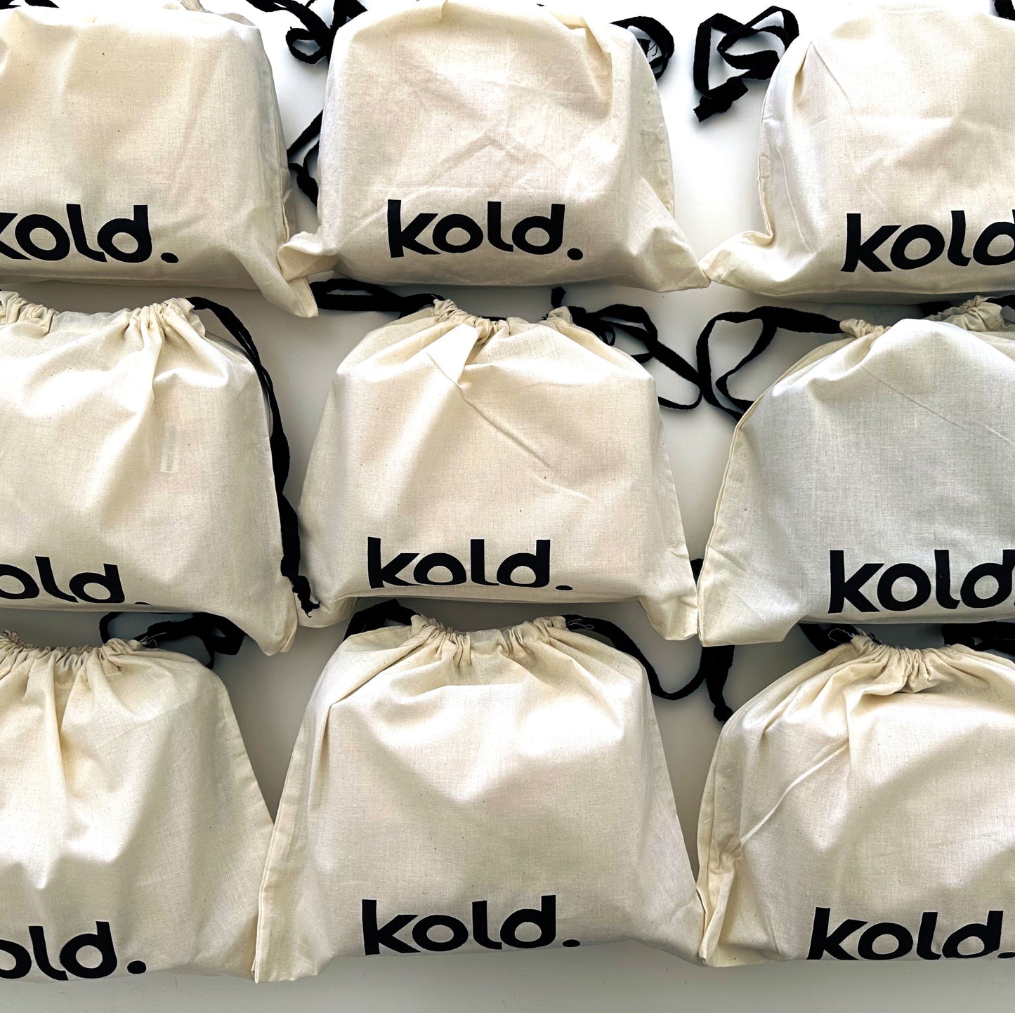 Multiple white and black drawstring bags with 'kold.' branding